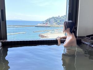 uma mulher sentada numa banheira com vista para o oceano em Grandview Atami Private Hot Spring Condominium Hotel em Atami
