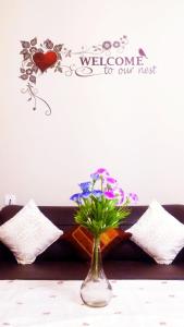 un jarrón con flores en una mesa con un cartel de bienvenida en Naadi Nest - 2 Bedroom Service Apartment, en Thanjāvūr