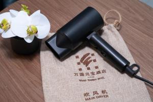 a black blow dryer next to a vase with white flowers at Guangzhou Wogo Yuanbao Hotel - Zhujiang New Town with free coffee in Guangzhou