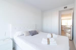 um quarto branco com uma grande cama branca e 2 toalhas em Global Properties, Apartamento con 2 terrazas en Gran Canet em Canet d'En Berenguer
