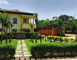 une maison jaune avec un banc et des palmiers dans l'établissement Riad Prince Louis, à Yaoundé