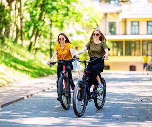 two women riding bikes down a street at Palangos Ramybės apartamentai in Palanga
