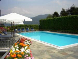 a swimming pool with an umbrella and some flowers at Hotel Adler in Menaggio
