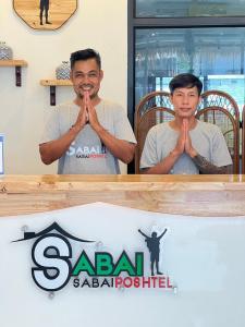 a man sitting in a table with his hands in front of a sign at Sabai Sabai Poshtel & Motorbike Rental in Ko Tao