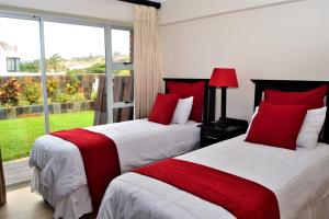 a bedroom with two beds with red pillows and a window at 26 Bronze Bay Umhlanga Rocks in Durban