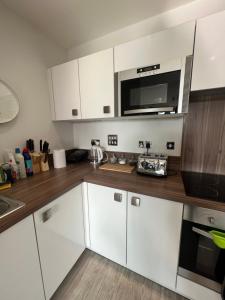 a kitchen with white cabinets and a microwave at Cityscape Serenity: 10th Floor Oasis near City Airport, Excel & 02 in London