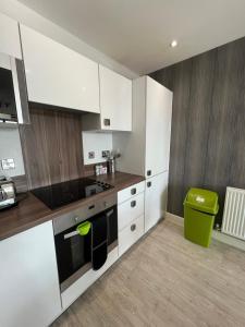 a kitchen with white cabinets and a green trash can at Cityscape Serenity: 10th Floor Oasis near City Airport, Excel & 02 in London