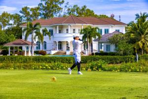 a man playing golf in front of a house at The White House, Palm Hills Golf and Country Club in Ban Nong Sai