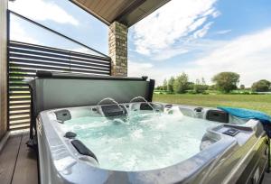 a hot tub on a deck with a view of a field at Stunning 3 Bed Lodge, Log Burner & Hot Tub with Lake View - Lakeside Lodge in Sturminster Marshall