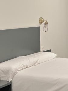 a bed with white sheets and a lamp on the wall at Apartamentos Lidar in Bilbao