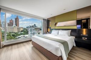 een slaapkamer met een groot bed en een groot raam bij Golden Tulip Mandison Suites in Bangkok