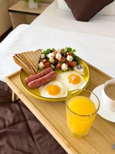 un piatto per la colazione con uova, salsicce, pane tostato e un bicchiere di succo di Apartment 5 a Almaty