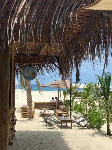 uma praia com um guarda-sol de palha e pessoas sentadas num banco em Secret Beach Hostel em Puerto Escondido
