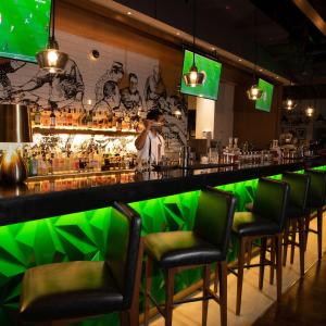 Um homem parado num bar com cadeiras verdes. em Hilton Doha The Pearl em Doha