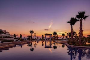 a pool with palm trees and a sunset in the background at Hilton Tangier Al Houara Resort & Spa in Al Houara