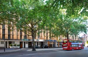 um autocarro vermelho a descer uma rua em frente a um edifício em Hilton London Kensington Hotel em Londres