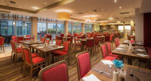 a restaurant with wooden tables and red chairs at Hilton Garden Inn Luton North in Luton