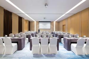 une salle de conférence avec des tables, des chaises et un écran dans l'établissement Hilton Garden Inn Qidong, à Qidong