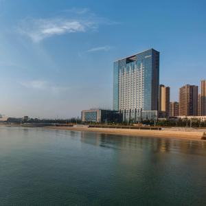 ein hohes Gebäude neben einem Wasserkörper in der Unterkunft Hilton Yantai Golden Coast in Yantai