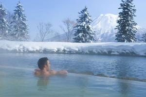 a man sitting in a hot tub in a snow covered lake at Hilton Niseko Village in Niseko
