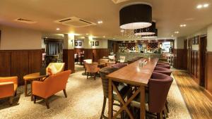 ストラトフォード・アポン・エイボンにあるDoubleTree by Hilton Stratford-upon-Avon, United Kingdomのバー、テーブル、椅子が備わるレストラン