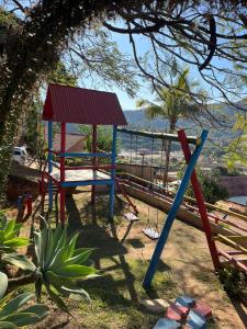 een speeltuin met een schommel in de schaduw van een boom bij Pousada 2 Baioco in Paty do Alferes
