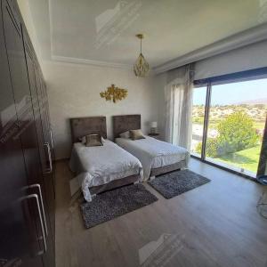 een slaapkamer met 2 bedden en een groot raam bij Sea Breeze Villa Taghazout Bay Amda golf & ocean view in Tamraght Ouzdar