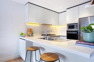 a kitchen with white cabinets and a sink and two stools at Urban Retreat in Surry Hills l 2 Bedroom Property with Parking in Sydney
