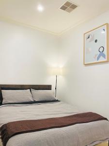 Bett in einem weißen Zimmer mit einem Bild an der Wand in der Unterkunft Bundled Bliss 2 bedroom Condo in Adelaide CBD in Adelaide