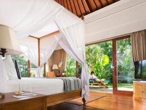 a bedroom in a villa with a bed and a woman sitting on a bench at The Shanti Residence by Elite Havens in Nusa Dua