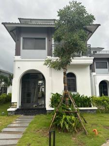 Una casa blanca con un árbol delante. en Lavender Sonasea Vân Đồn, Quảng Ninh en Quang Ninh