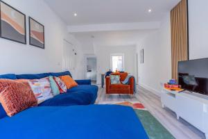 Charming 3 BR in Folkestone! في فولكستون: غرفة معيشة مع أريكة زرقاء وتلفزيون بشاشة مسطحة