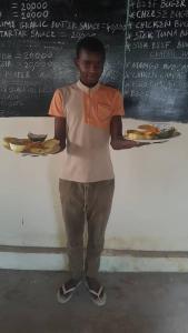 a boy standing in front of a chalkboard with plates of food at Stonefish Inn Jambiani in Jambiani