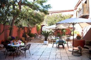 un patio extérieur avec des tables, des chaises et un parasol dans l'établissement Baglio Buccellato, à Scopello