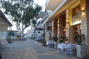 Miss Nefeli - Marvelous Stone Apartment in Perdika-Aegina في ايجينا تاون: شارع فارغ فيه طاولات وكراسي خارج المبنى