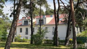 biały dom z czerwonym dachem i drzewami w obiekcie Apartamenty Sun & Snow Sosnowy Zakątek w mieście Mrzeżyno