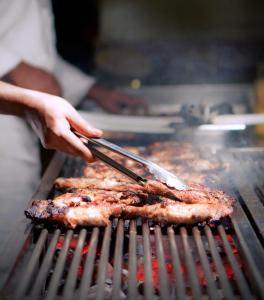 a person cooking meat on a grill with tongs at Ocean Paradise Hotel and Resort in Cox's Bazar