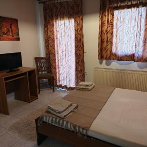 a bedroom with a bed and a desk and two windows at Anilio Rooms in Anilio Metsovo
