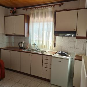 cocina con armarios blancos, fregadero y ventana en Anilio Rooms, en Anilio - Metsovo
