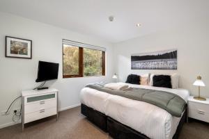 a white bedroom with two beds and a television at Snow Stream 3 Bedroom and loft with gas fire garage parking and balcony in Thredbo