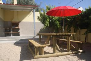 a picnic table with a red umbrella and a bench at CasaTioManel in Amiães de Baixo