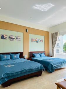1 dormitorio con 2 camas con sábanas azules y ventana en Bình Minh Motel en Pleiku