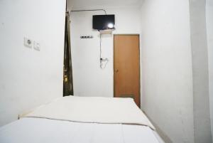 Cama blanca en habitación con TV en la pared en Griya Sawamah Syariah Mitra RedDoorz, en Yakarta