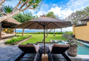 een patio met een parasol en stoelen naast een zwembad bij AYANA Villas Bali in Jimbaran