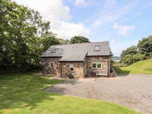 a stone house on a hill with a gravel driveway at Traeth Ora in Penrhos-Lligwy