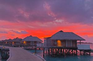 a pier with huts on the water at sunset at Six Senses Laamu in Laamu Atoll