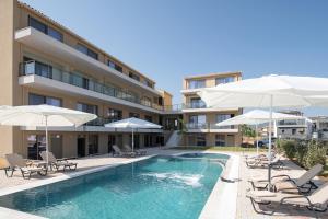 a swimming pool with chairs and umbrellas next to a building at Aetherion Studios & Suites in Kalivia Poligirou