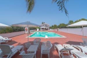 een zwembad met stoelen, een tafel en een parasol bij Appartamento con vista piscina in Noto