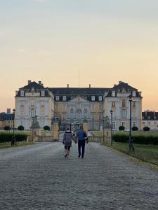 zwei Personen, die vor einem großen Gebäude eine Straße entlang gehen in der Unterkunft Apartment am Schloss in Brühl