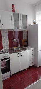 La cuisine est équipée de placards blancs, d'un évier et d'un réfrigérateur. dans l'établissement Apartman 'CENTAR', à Kula